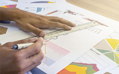 Manos de hombre con bolígrafo escribiendo sobre hojas con gráficos.